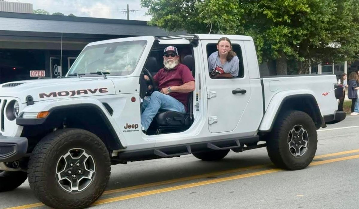 Bo’s retirement toy A white Jeep Gladiator Mojave with its doors removed is parked on a street. An older man with a white beard and sunglasses is in the driver’s seat, and a woman leans out from the passenger side. Trees and a building are in the background.