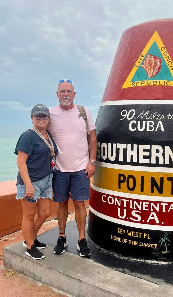Patty (wife) and Bo Higginbotham A man and woman pose in front of the Southernmost Point Buoy in Key West, Florida, which marks 90 miles to Cuba; the ocean and cloudy sky are visible in the background.